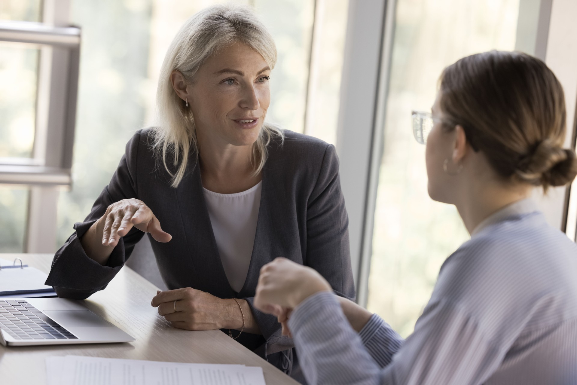 Two young and mature business colleagues women talking at table
